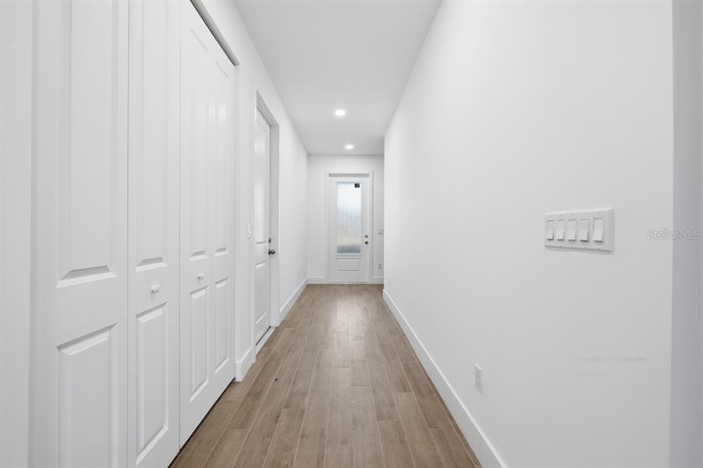A hallway with white walls, wood-look tile flooring, and a door at the end — 500 SUNSET ROAD N, ROTONDA WEST, FL