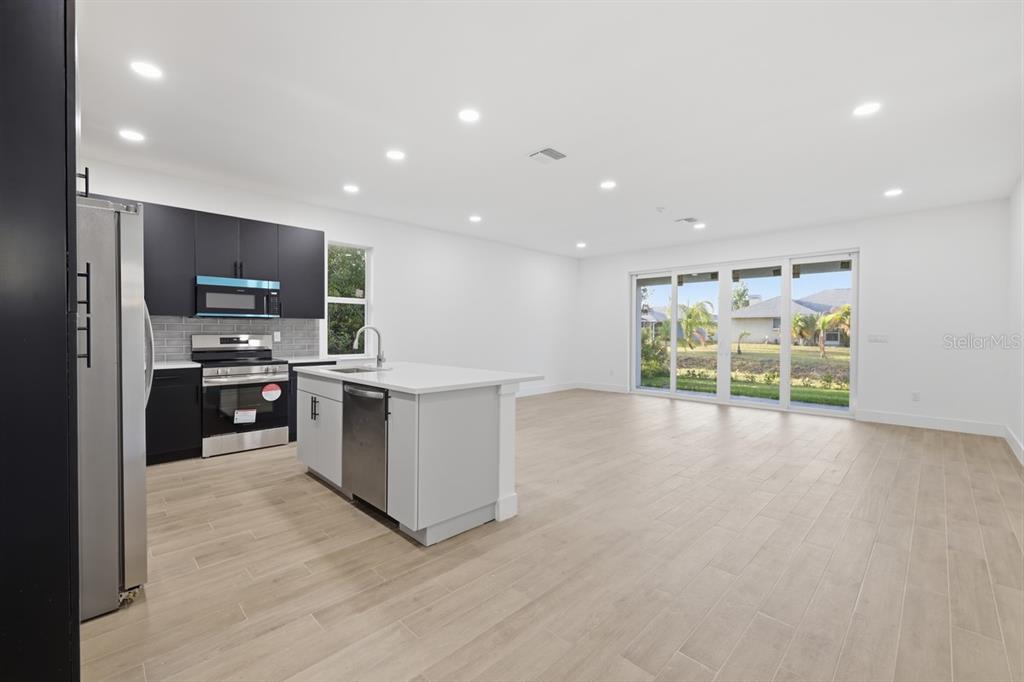 A modern kitchen with black cabinets and a white island opens to a spacious living area — 500 SUNSET ROAD N, ROTONDA WEST, FL