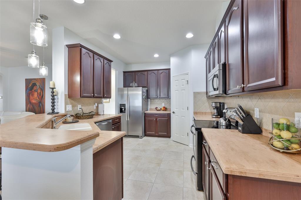 A kitchen features dark wood cabinets, light countertops, stainless steel appliances, and tile flooring — 823 SEMINOLE SKY DRIVE, RUSKIN, FL