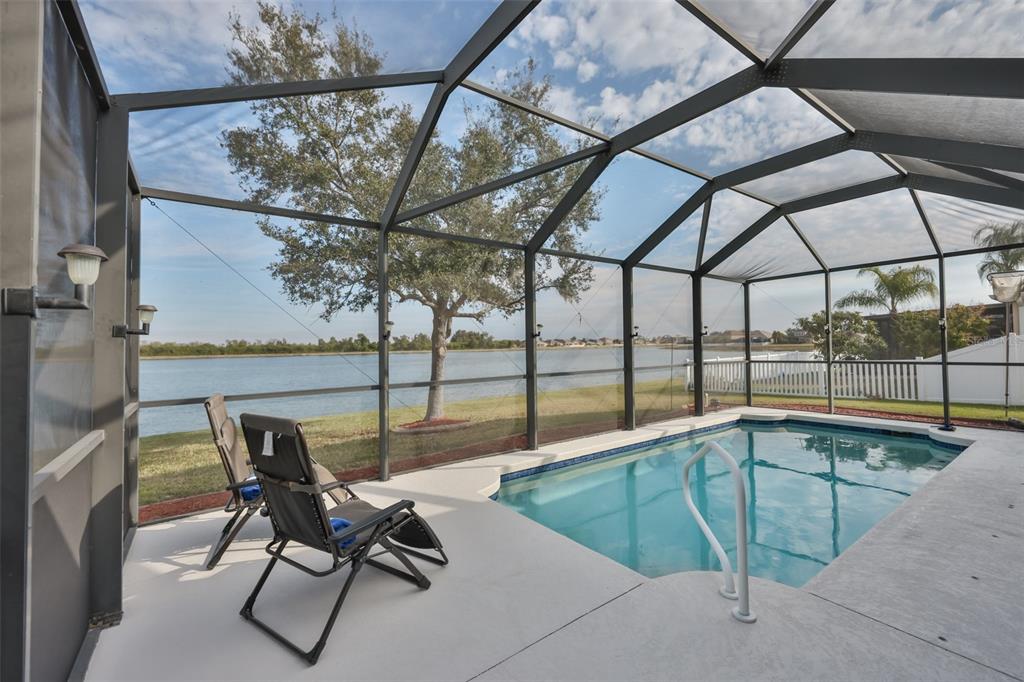 A screened-in pool patio overlooks a lake with two lounge chairs on the concrete deck — 823 SEMINOLE SKY DRIVE, RUSKIN, FL