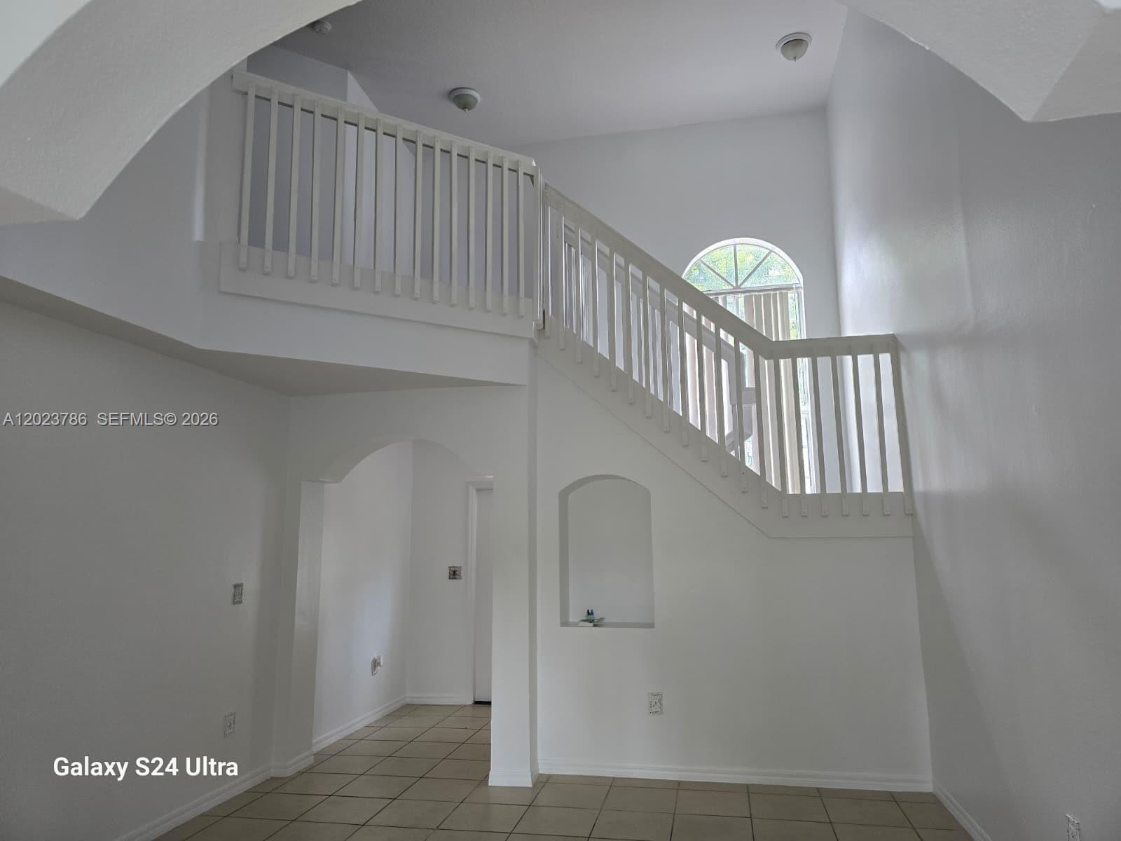A white interior features a staircase with a wooden railing and an arched wall niche — 13658 SW 142nd Ter # 13658, Miami FL 33186, MIAMI, FL