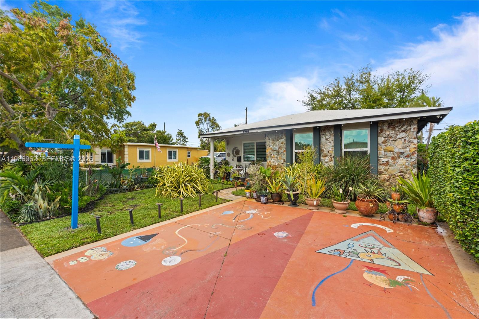 A stone-faced house features a painted driveway and a variety of potted plants — 720 NW 4th St, Hallandale Beach FL 33009, HALLANDALE BEACH, FL
