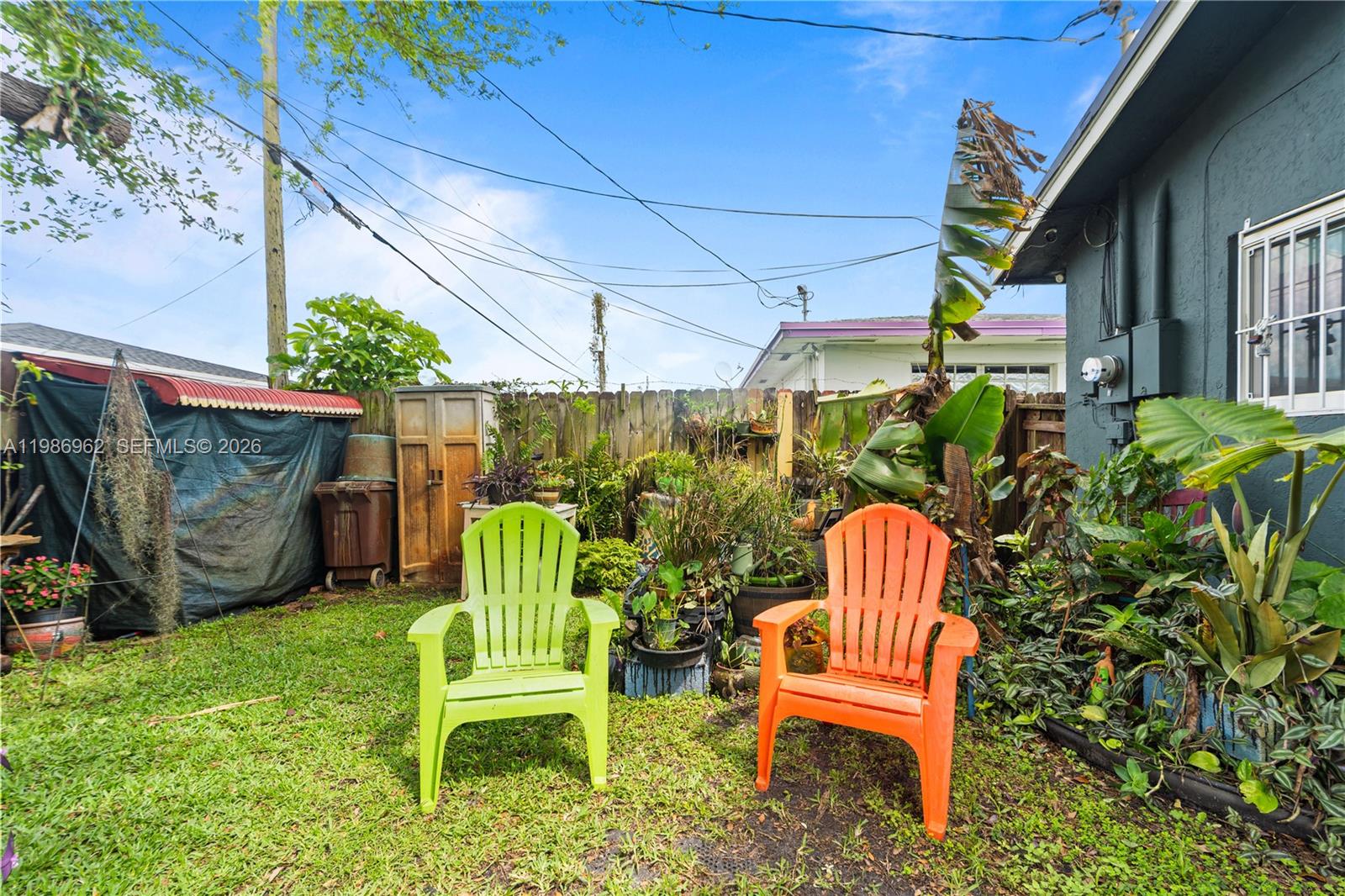 A backyard features a green chair, an orange chair, potted plants, and a wooden fence — 720 NW 4th St, Hallandale Beach FL 33009, HALLANDALE BEACH, FL