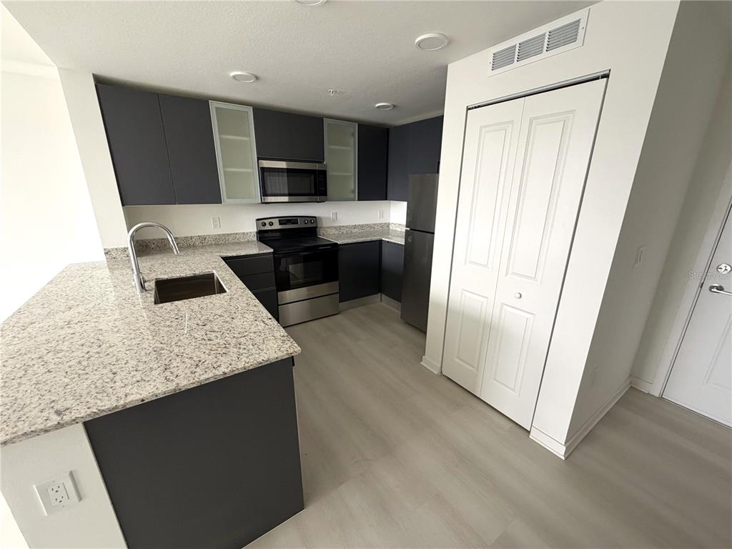 A kitchen features dark cabinets, granite countertops, stainless steel appliances, and light wood-look flooring — 5587 MILLENIA PARK BLVD UNIT 303, ORLANDO, FL