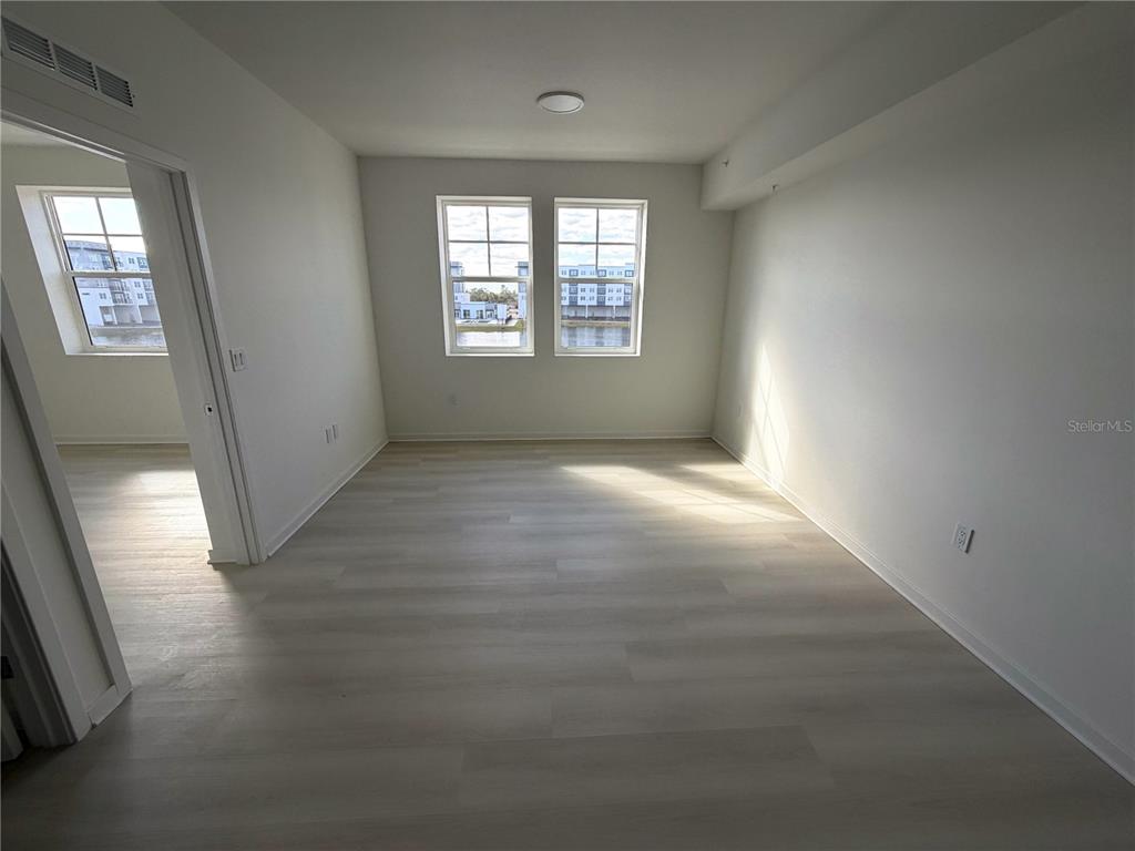 An empty room with light wood-look flooring, white walls, and two windows overlooking a building — 5587 MILLENIA PARK BLVD UNIT 303, ORLANDO, FL
