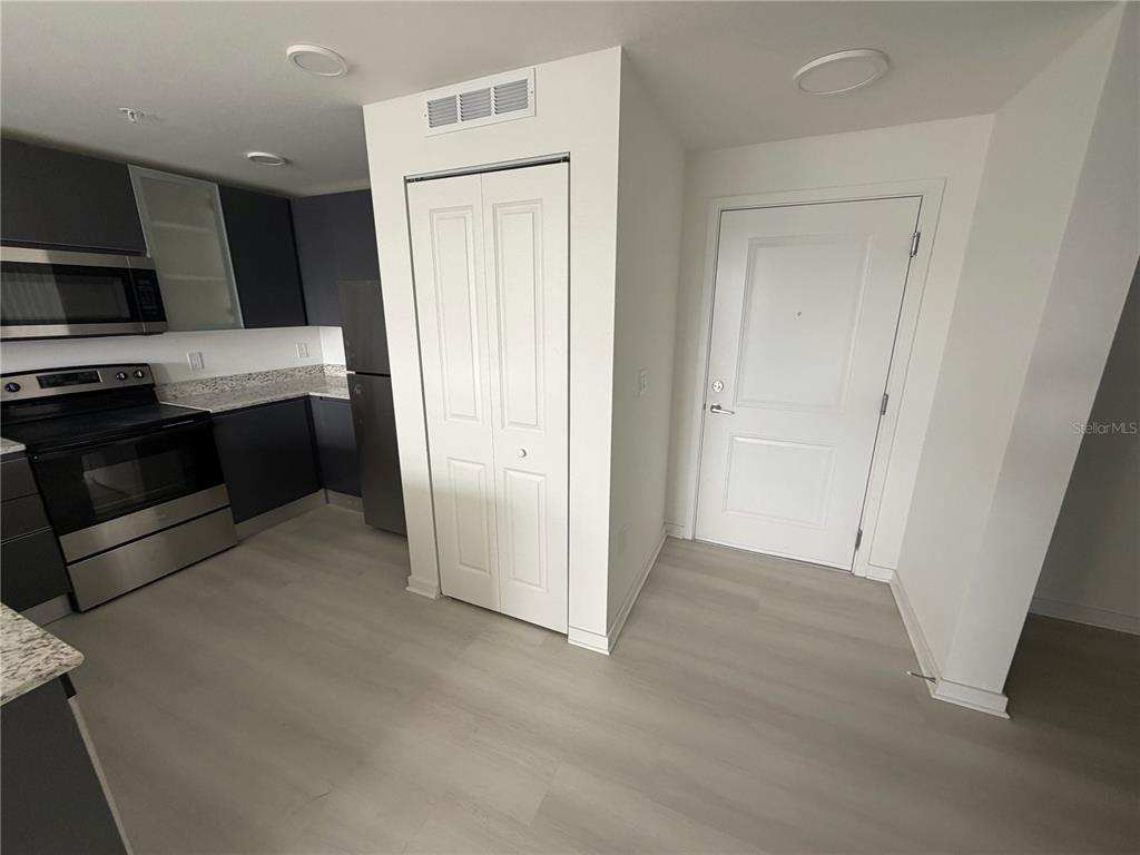 A kitchen with dark cabinets, stainless steel appliances, and light flooring next to a closet — 5587 MILLENIA PARK BLVD UNIT 303, ORLANDO, FL