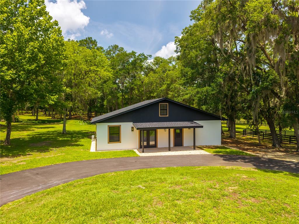 A modern, single-story house with white walls and dark siding sits on a grassy lot — 6450 NW HIGHWAY 225, OCALA, FL