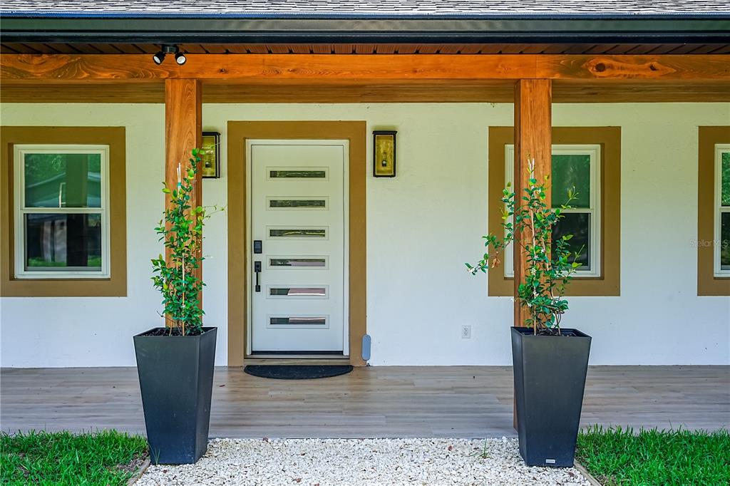 A white front door with horizontal glass panels sits on a porch with two planters — 6450 NW HIGHWAY 225, OCALA, FL