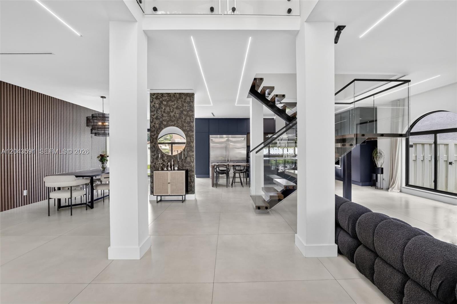 A modern open-concept living area features a floating staircase, tiled floors, and white columns — 10746 Charleston Pl, Cooper City FL 33026, COOPER CITY, FL