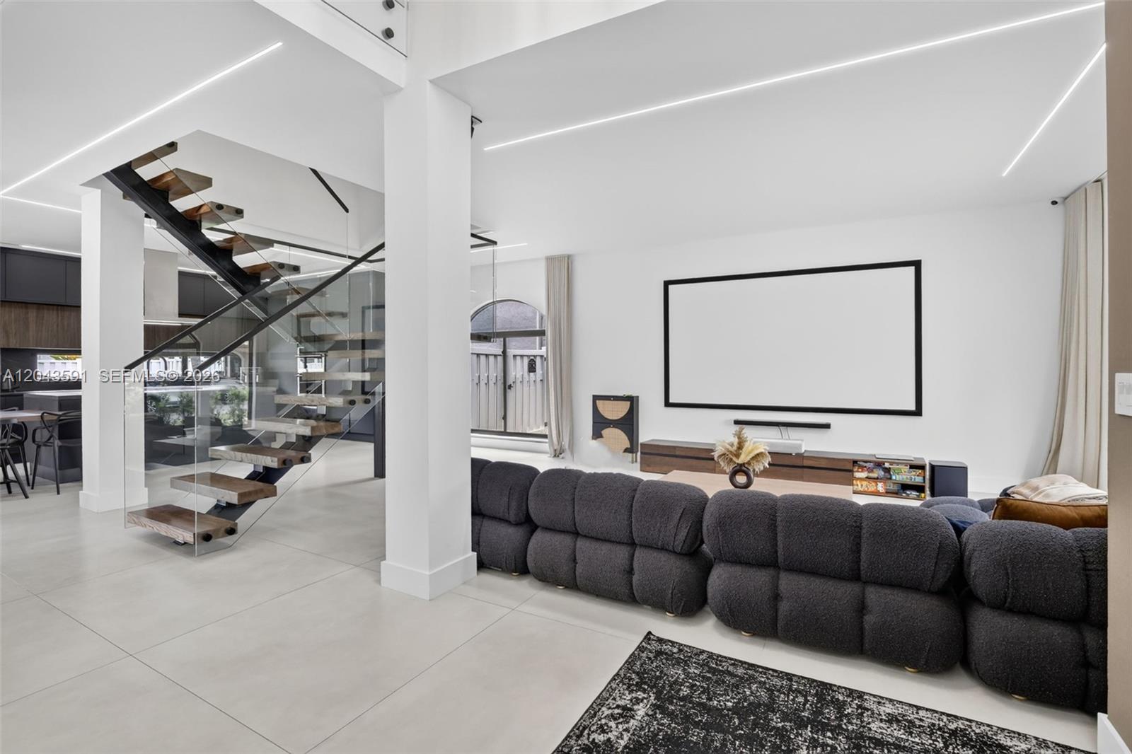 A modern living room features a floating staircase, a large projector screen, and dark furniture — 10746 Charleston Pl, Cooper City FL 33026, COOPER CITY, FL