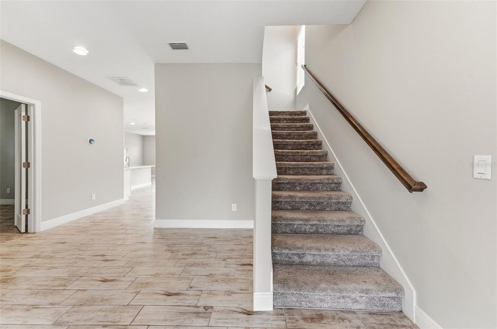 A staircase with gray carpet leads upward next to a room with wood-look tile flooring — 3940 MAURICE AVENUE, ODESSA, FL