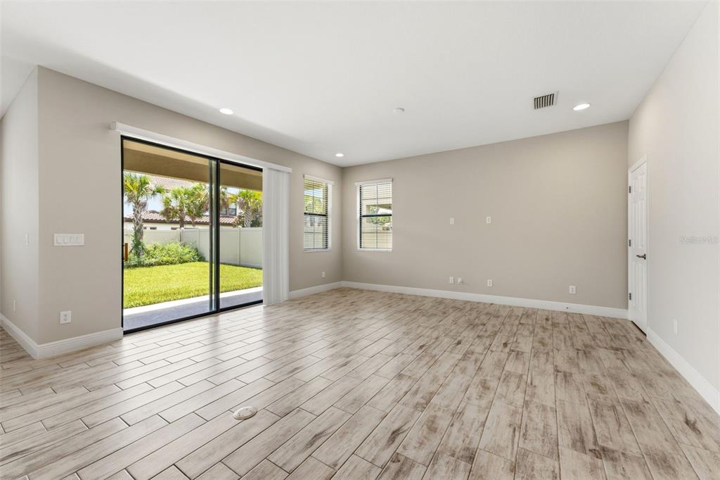 An empty living room features light wood-look tile flooring, beige walls, and a sliding glass door — 3940 MAURICE AVENUE, ODESSA, FL