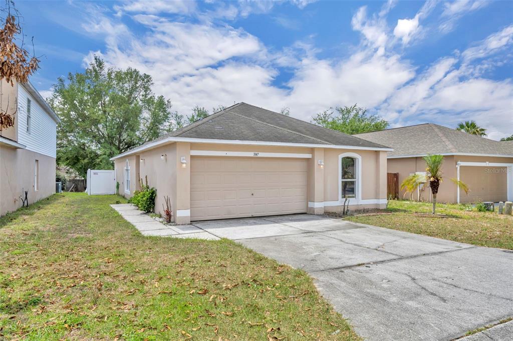 A single-story house with a tan stucco exterior, a two-car garage, and a concrete driveway — 3147 WHISPERING TRAILS STREET, WINTER HAVEN, FL