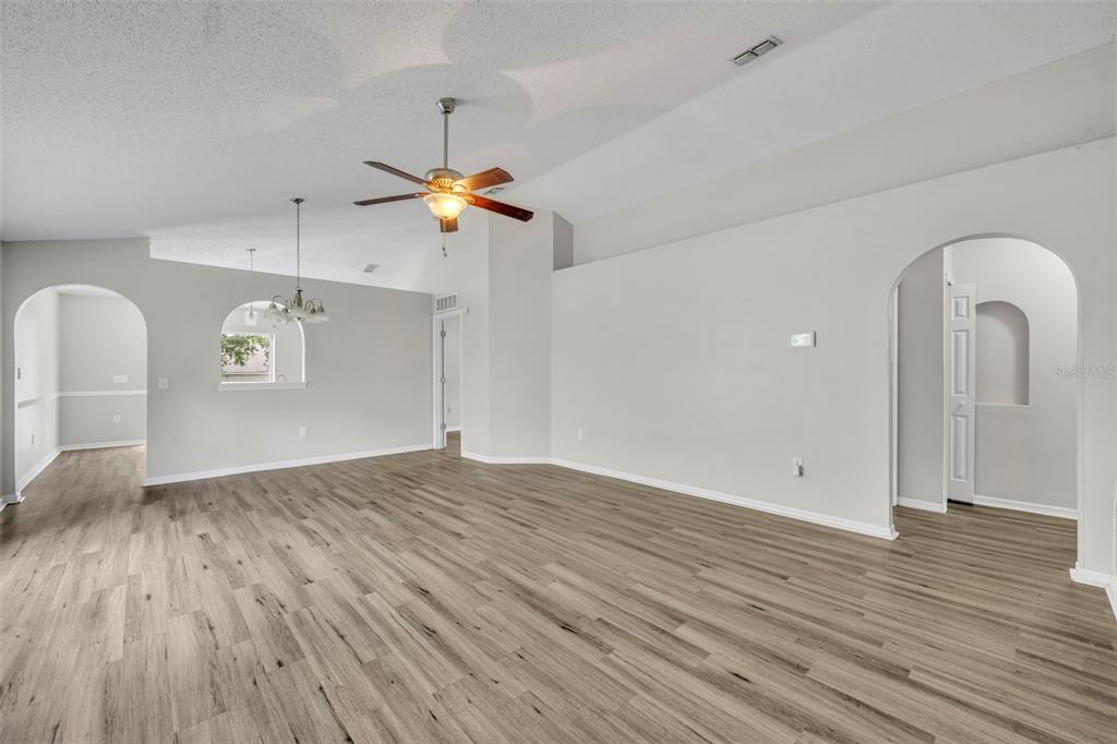 An empty living room features light gray walls, wood-look flooring, and a vaulted ceiling — 3147 WHISPERING TRAILS STREET, WINTER HAVEN, FL