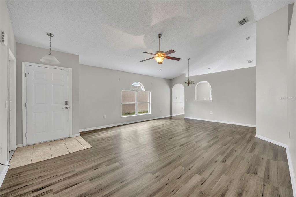 An open-concept living area features light gray walls, wood-look flooring, a ceiling fan, and arched doorways — 3147 WHISPERING TRAILS STREET, WINTER HAVEN, FL