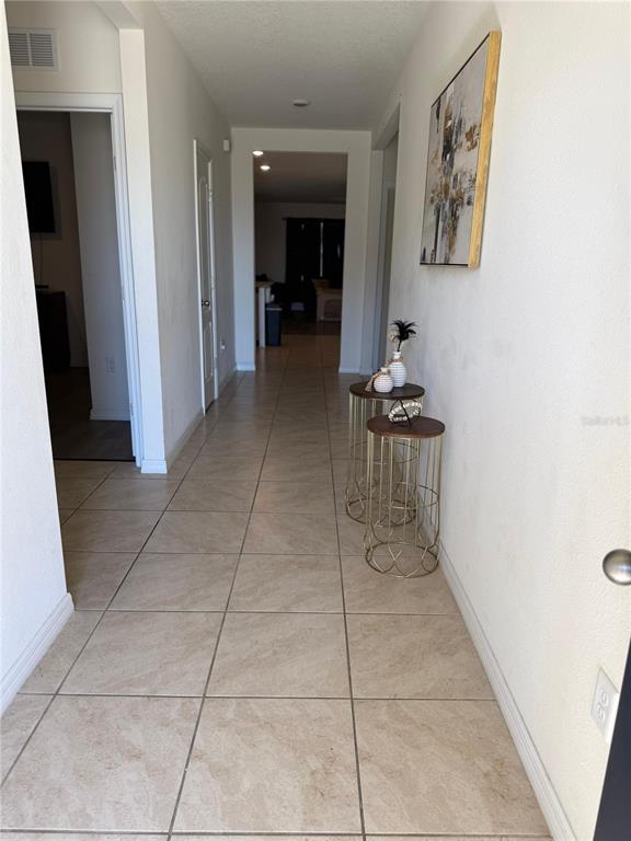 A hallway with light-colored tile flooring leads to an open living area — 784 SILVER PALM DRIVE, HAINES CITY, FL