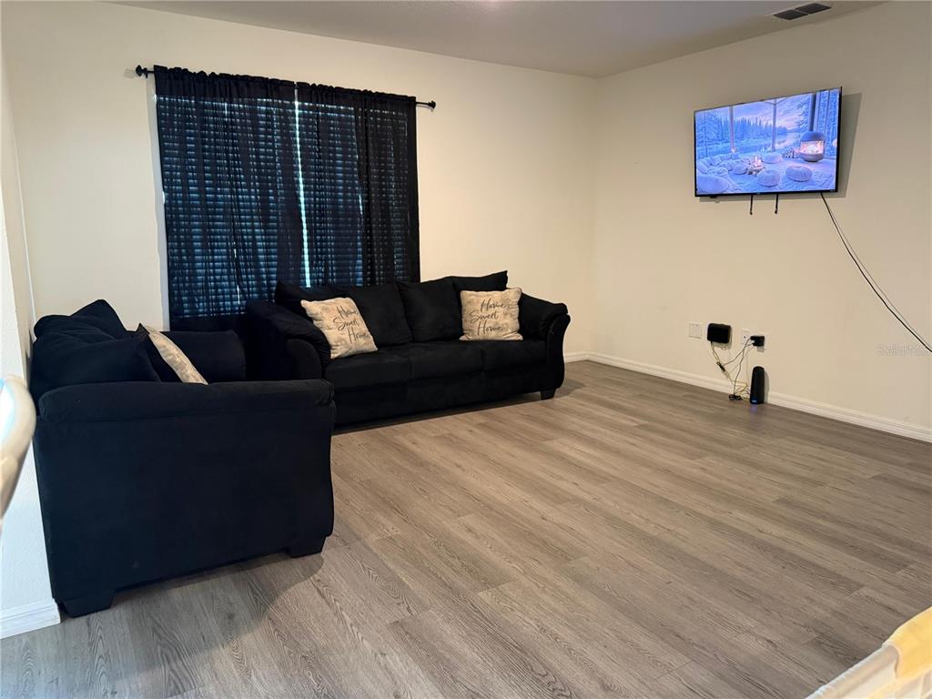 A living room features light wood-look flooring, black furniture, and a wall-mounted television — 784 SILVER PALM DRIVE, HAINES CITY, FL