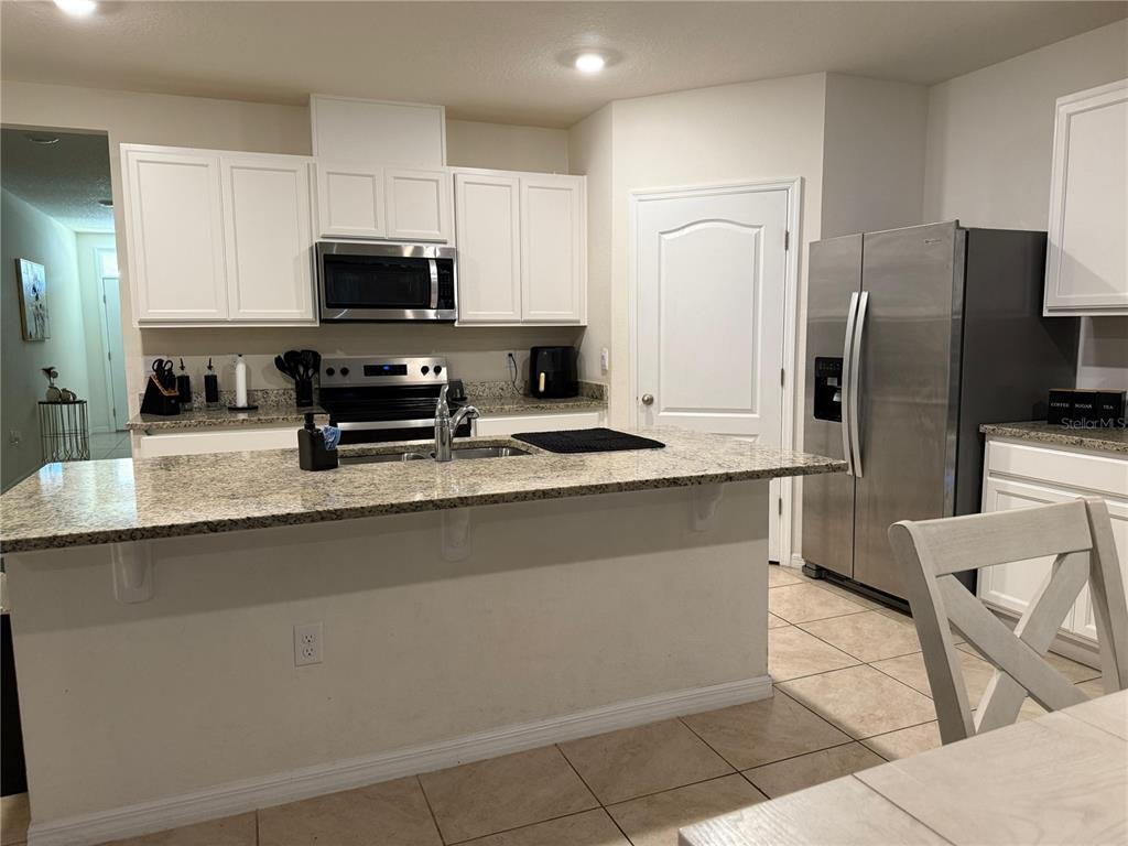 A kitchen features white cabinets, granite countertops, a center island, and stainless steel appliances — 784 SILVER PALM DRIVE, HAINES CITY, FL