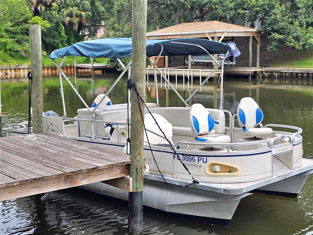 A pontoon boat with a blue canopy is docked at a wooden pier on water — 10 FANWOOD COURT, PALM COAST, FL