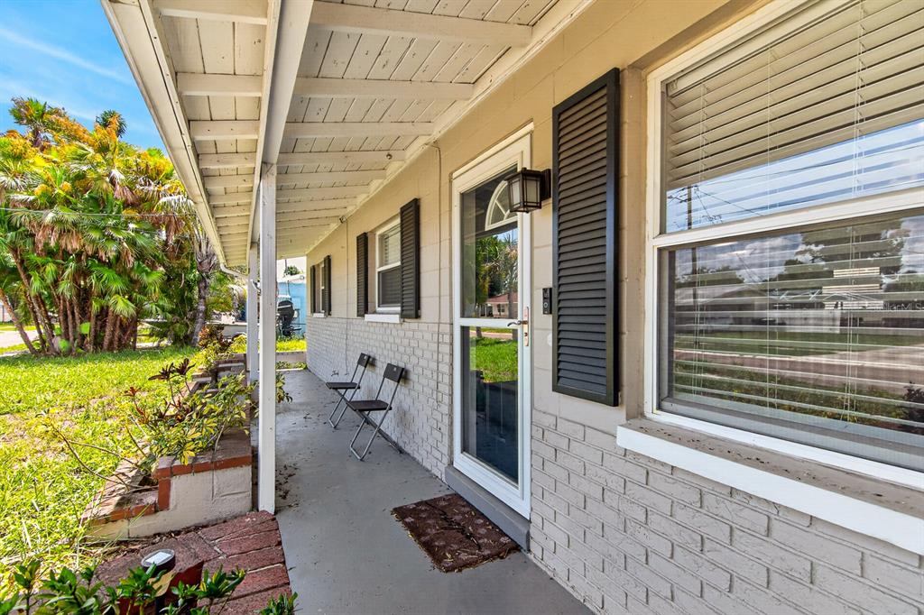 A covered concrete porch with brick planters, two folding chairs, and a front door — 4014 W LAND AVENUE, TAMPA, FL