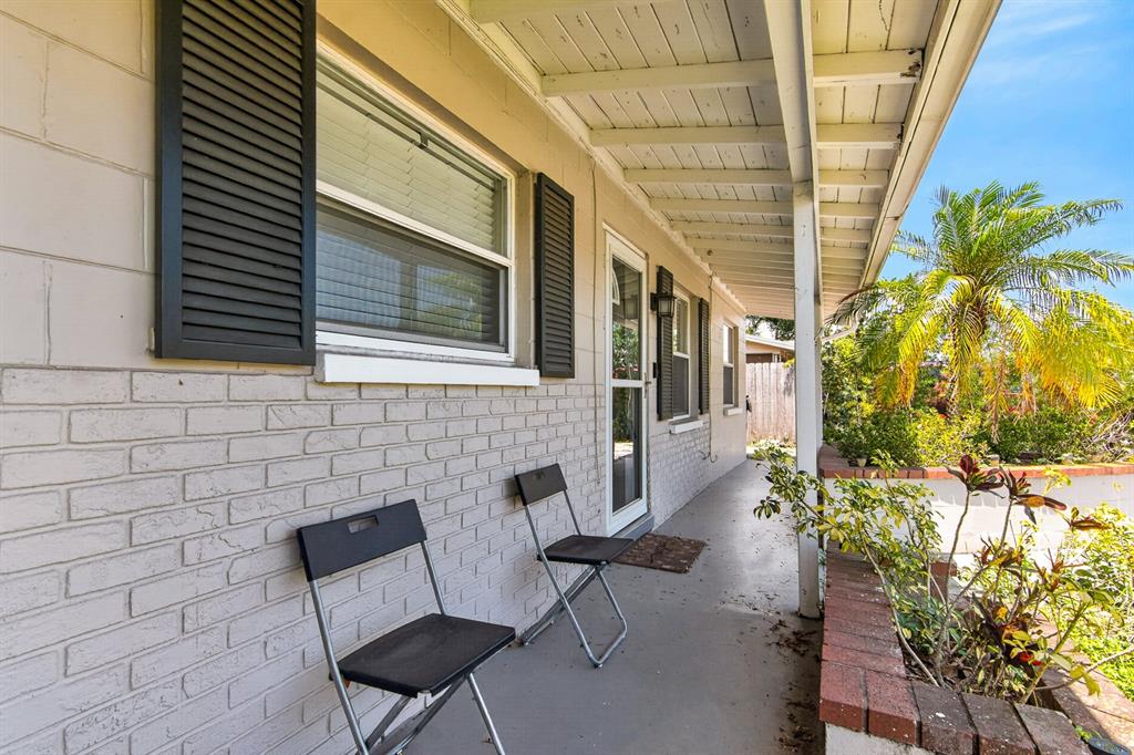 A covered porch features a brick wall, two black folding chairs, and a brick planter — 4014 W LAND AVENUE, TAMPA, FL