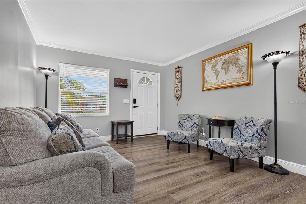 A living room features gray walls, wood-look flooring, a gray sofa, and two patterned chairs — 4014 W LAND AVENUE, TAMPA, FL