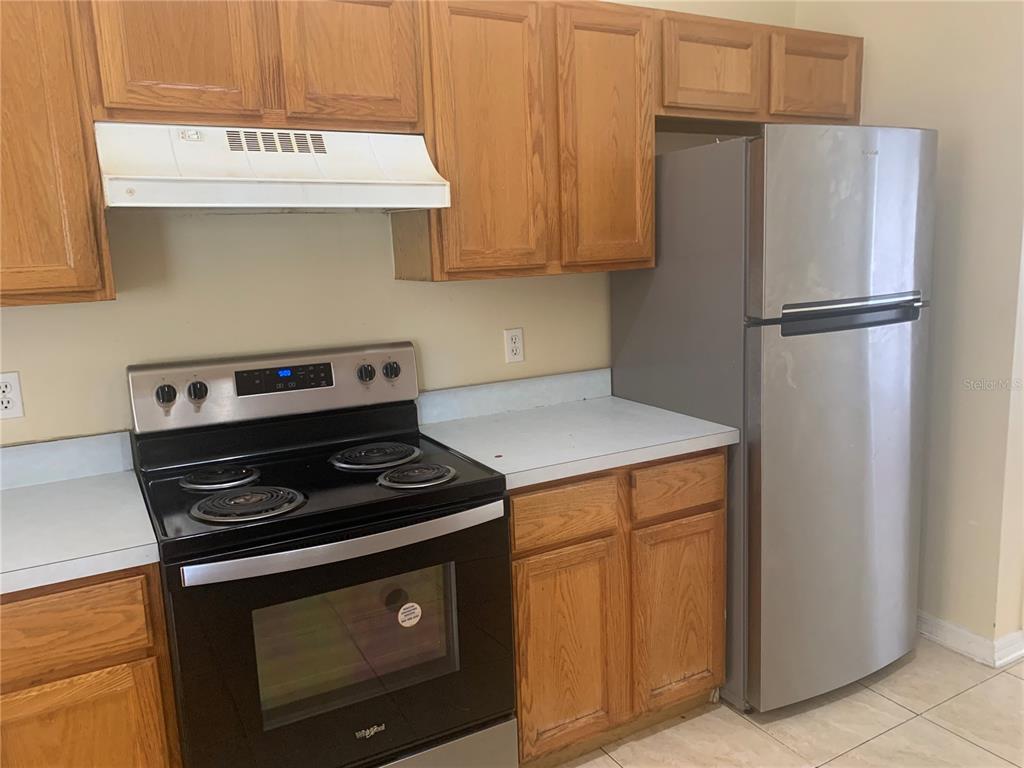 A kitchen features wood cabinets, a black electric stove, and a stainless steel refrigerator — 11941 HATCHER CIRCLE, ORLANDO, FL