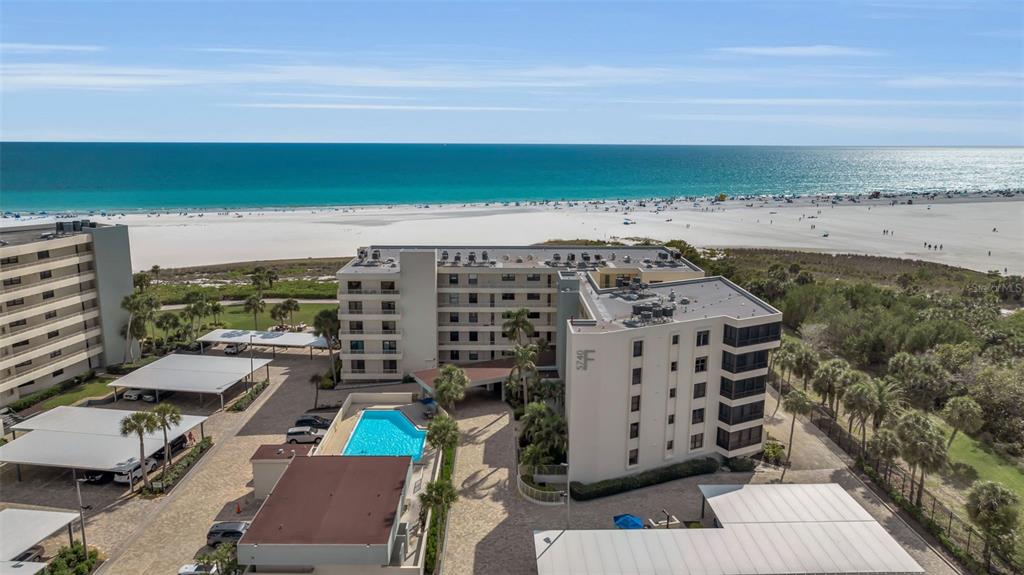 An aerial view shows a multi-story beachfront condominium complex with a pool and parking structures — 5740 MIDNIGHT PASS ROAD UNIT 403, SARASOTA, FL
