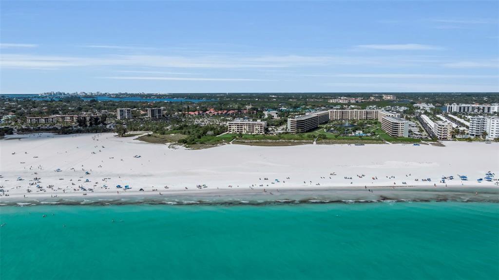 An aerial view shows a white sand beach bordering turquoise water with several large apartment buildings — 5740 MIDNIGHT PASS ROAD UNIT 403, SARASOTA, FL