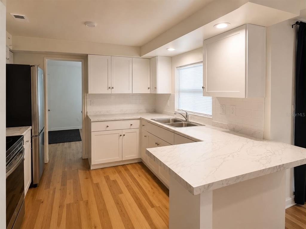 A kitchen with white cabinets, marble-look countertops, stainless steel appliances, and light wood flooring — 3115 LOCKWOOD MEADOWS BOULEVARD, SARASOTA, FL