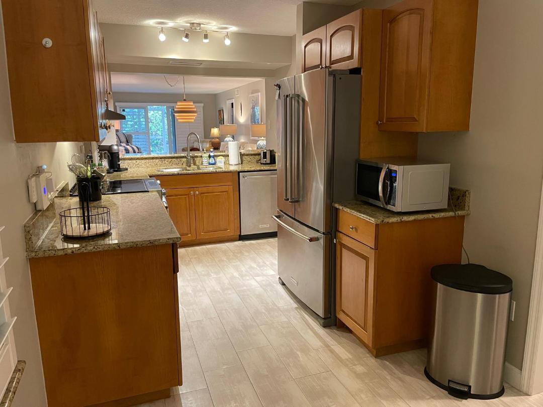 A kitchen with wood cabinets, granite countertops, stainless steel appliances, and light-colored tile flooring — 10980 S Ocean Drive # 111, Jensen Beach FL 34957, JENSEN BEACH, FL