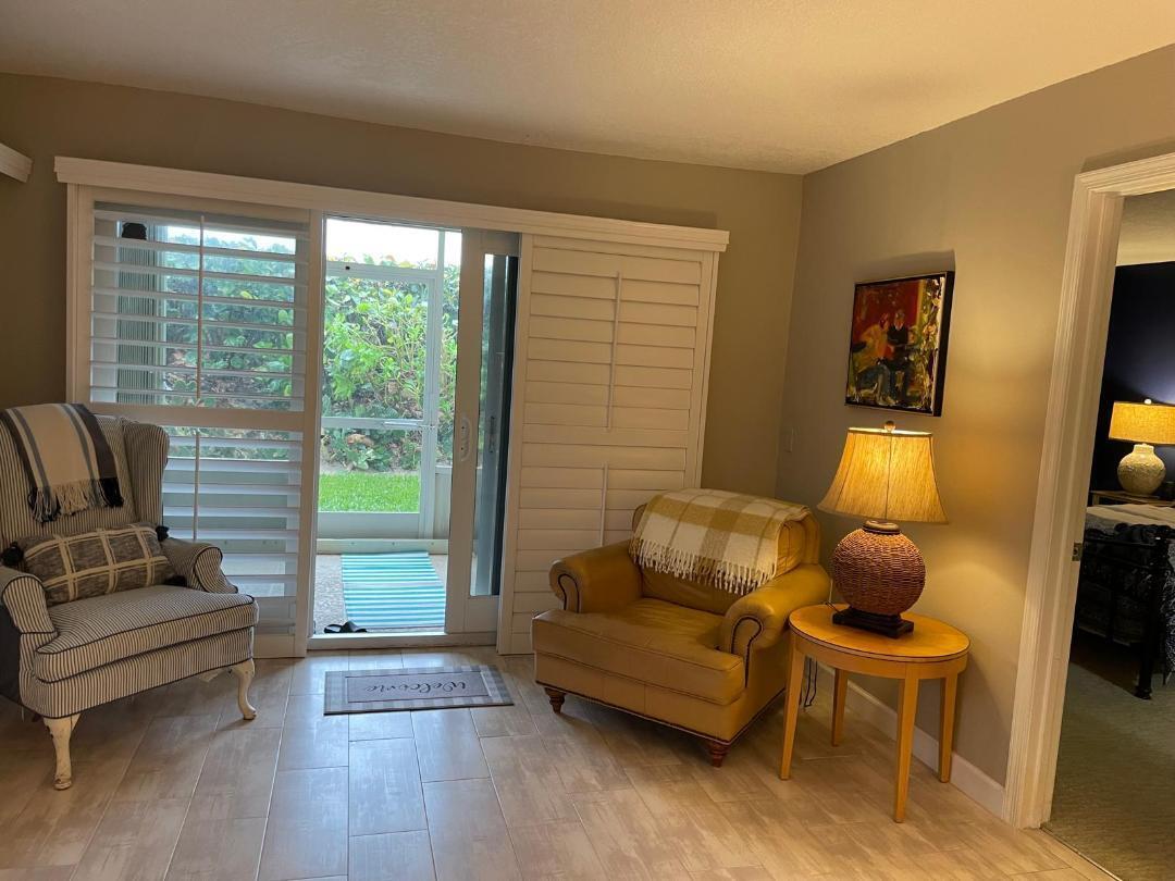 A sunlit room features two armchairs, a side table with a lamp, and sliding glass doors — 10980 S Ocean Drive # 111, Jensen Beach FL 34957, JENSEN BEACH, FL