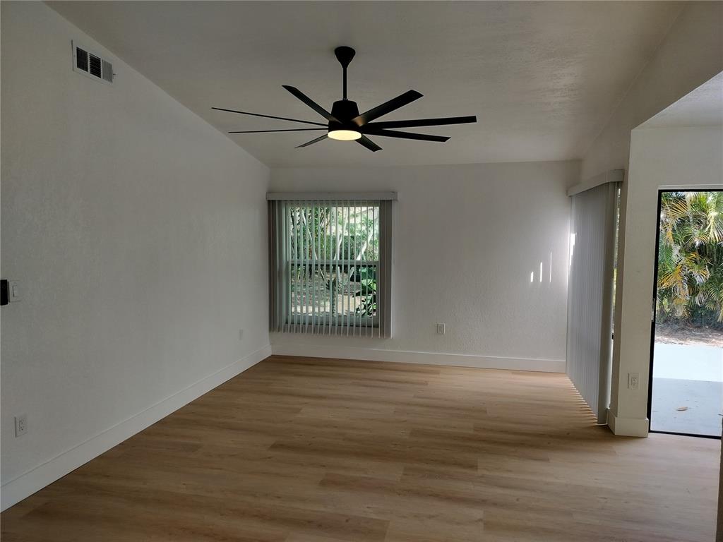 An empty room features light wood-look flooring, a modern ceiling fan, and vertical window blinds — 2661 WARMSPRINGS WAY, PALM HARBOR, FL
