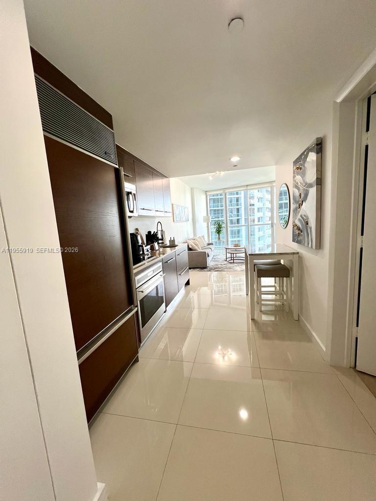 A modern kitchen with dark wood cabinetry leads into a bright living area with floor-to-ceiling windows — 495 Brickell Ave # 3208, Miami FL 33131, MIAMI, FL
