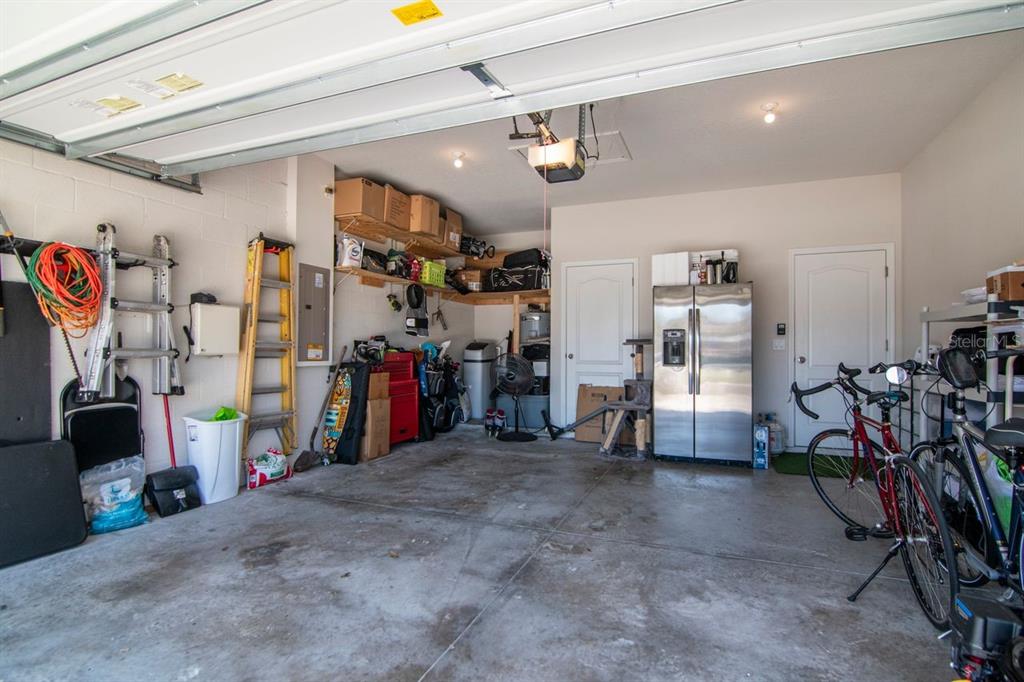 A garage with concrete floors, storage shelving, a refrigerator, and two bicycles parked inside — 10455 HERON HIDEAWAY LOOP, LAND O LAKES, FL