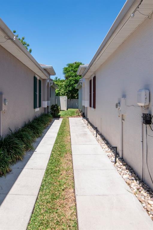 A narrow concrete walkway with a central grass strip runs between two residential exterior walls — 10455 HERON HIDEAWAY LOOP, LAND O LAKES, FL