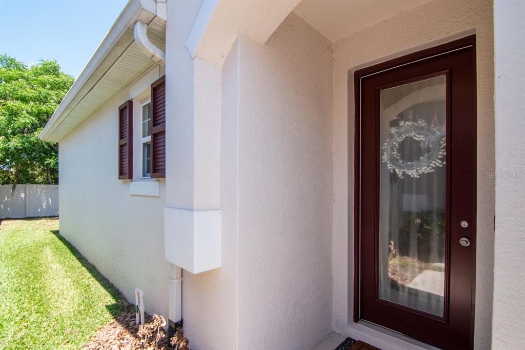 A side view of a house exterior featuring a dark red front door and window — 10455 HERON HIDEAWAY LOOP, LAND O LAKES, FL