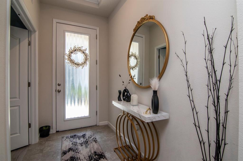 An entryway features a white door, a marble-topped console table, and a gold-framed oval mirror — 10455 HERON HIDEAWAY LOOP, LAND O LAKES, FL