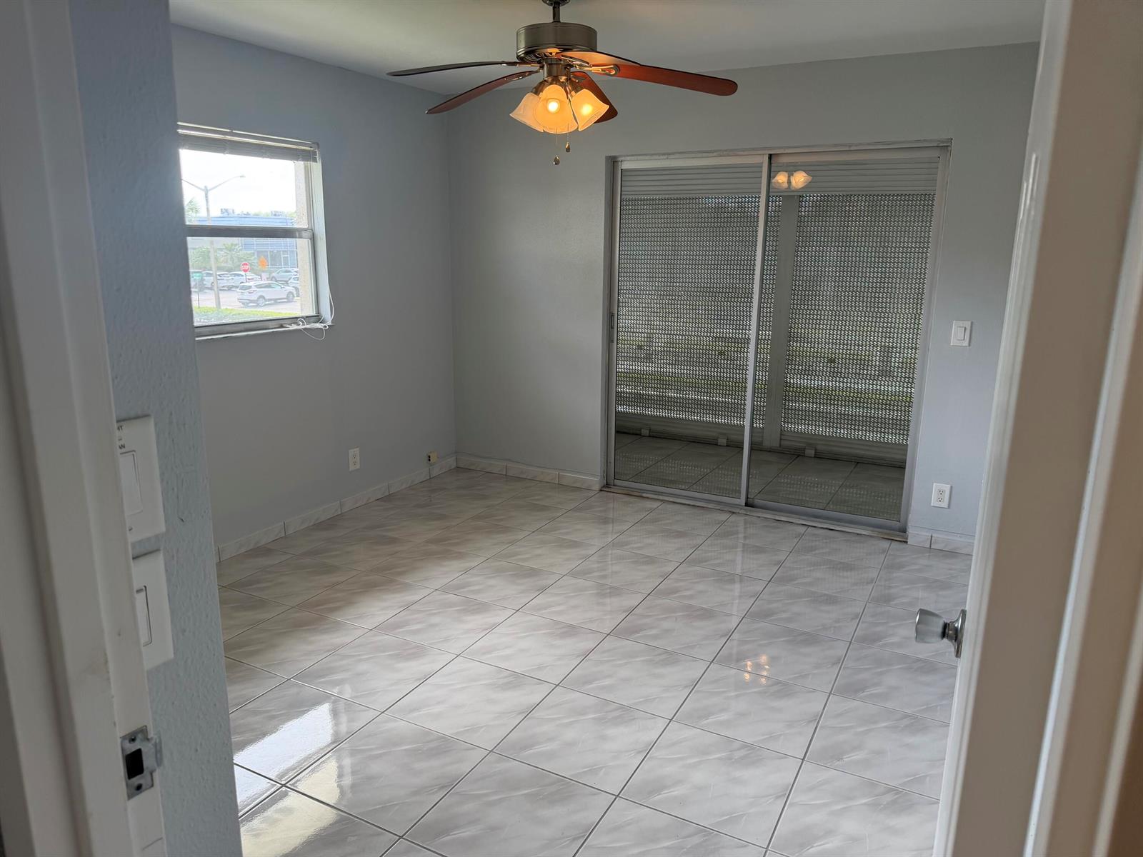 An empty room features light gray walls, white tile flooring, a ceiling fan, and sliding doors — 373 Monaco H, # H, Delray Beach FL 33446, DELRAY BEACH, FL