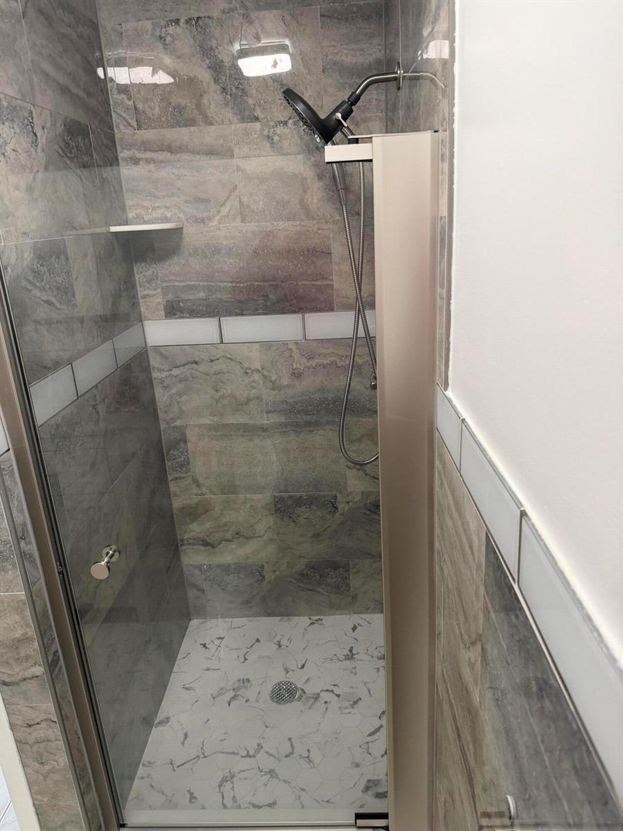 A walk-in shower features gray stone-look wall tiles, a white marble-patterned floor, and glass doors — 373 Monaco H, # H, Delray Beach FL 33446, DELRAY BEACH, FL