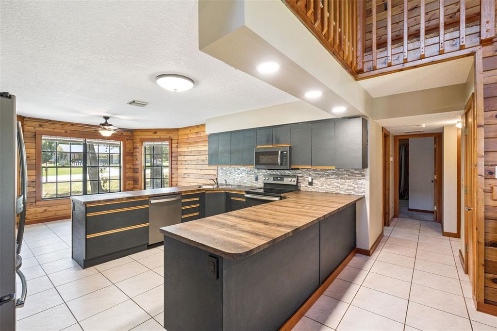 A living room with wood-paneled walls, a loft, a staircase, and tiled floors — 25911 ABERDOVEY AVENUE, SORRENTO, FL