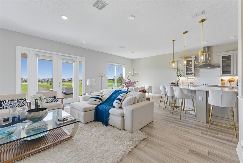 An open-concept living room and kitchen feature light wood floors, white furniture, and gold lighting — 5211 CITRUS LEAF BOULEVARD, WINTER GARDEN, FL