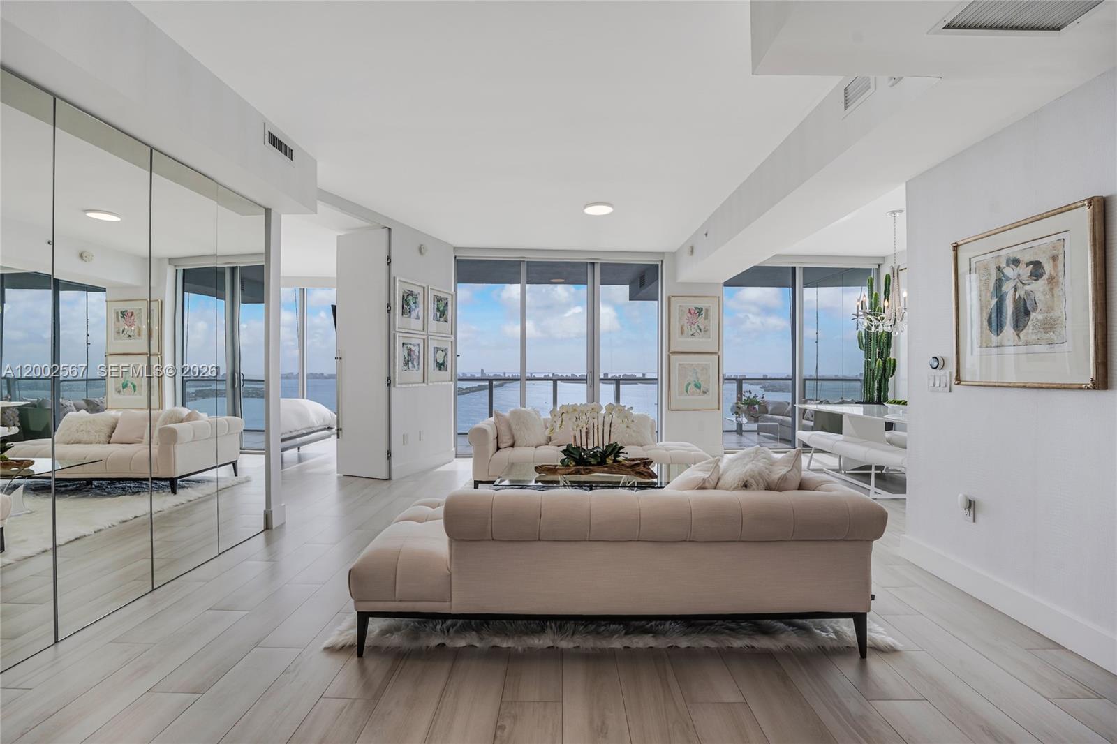 A bright living room features light wood floors, tufted sofas, and floor-to-ceiling windows overlooking water — 2900 NE 7th Ave # 4003, Miami FL 33137, MIAMI, FL