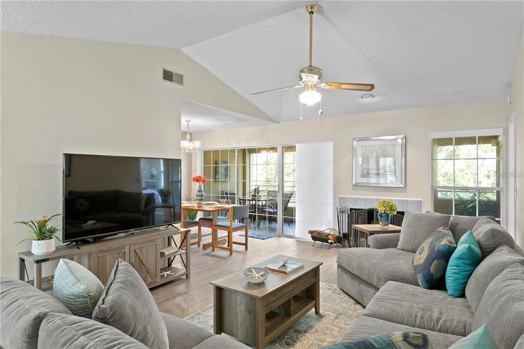 A living room with a vaulted ceiling, gray sectional sofa, television, and dining area beyond — 10823 INDIAN HILLS COURT UNIT 33, SEMINOLE, FL