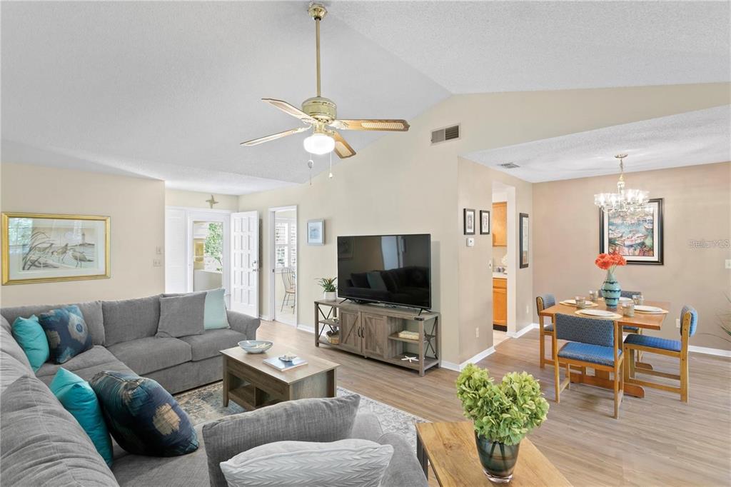 An open-concept living and dining area features a vaulted ceiling, gray sectional, and wood flooring — 10823 INDIAN HILLS COURT UNIT 33, SEMINOLE, FL