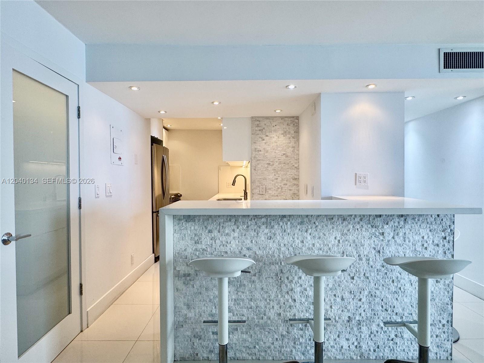 A kitchen features a white stone-tiled breakfast bar with three stools and recessed lighting — 200 SE 15th Rd # 9I, Miami FL 33129, MIAMI, FL