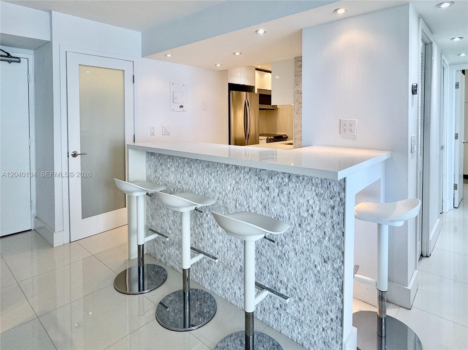 A kitchen island with a stone-tiled front and four white bar stools sits in a room — 200 SE 15th Rd # 9I, Miami FL 33129, MIAMI, FL