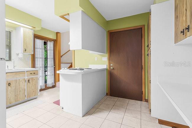 A kitchen features light wood cabinets, a white peninsula with a stovetop, and tile flooring — 7360 CHERRY LAUREL DRIVE, ORLANDO, FL