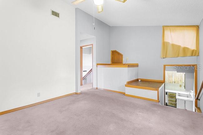 A carpeted room features a raised platform, wood trim, and a view into a kitchen — 7360 CHERRY LAUREL DRIVE, ORLANDO, FL