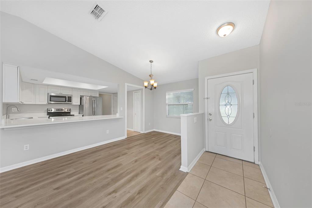 An open-concept dining area features light wood-look flooring, a kitchen pass-through, and an entryway door — 224 WHISPER LAKE ROAD, PALM HARBOR, FL